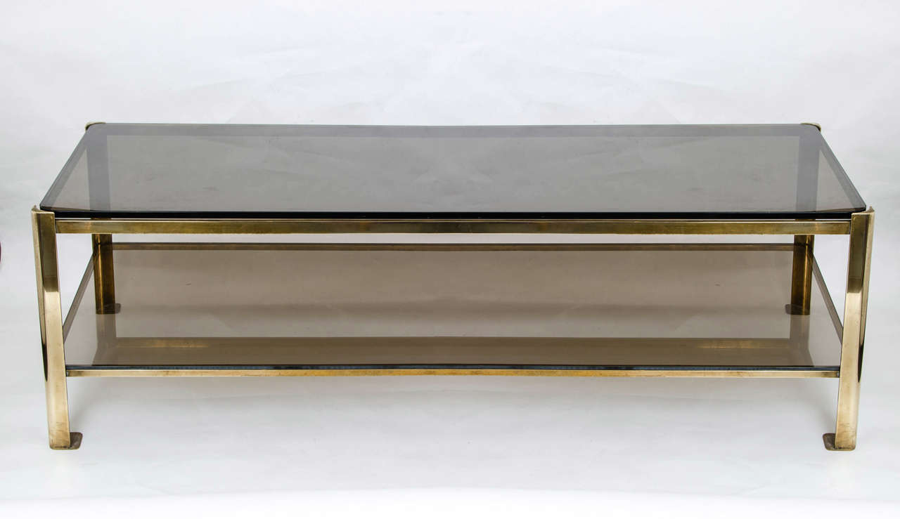 Classic 1950s two-tiered coffee table by Jacques Quinet (French) in brass with smoked glass tops, beautifully curved corners and free-flowing proportions, an amalgam of elegance and minimalism.

Jacques Quinet's career spanned five decades