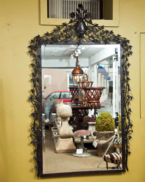 Black iron mirror boasts detail work of cascading ivy from vase of flowers.