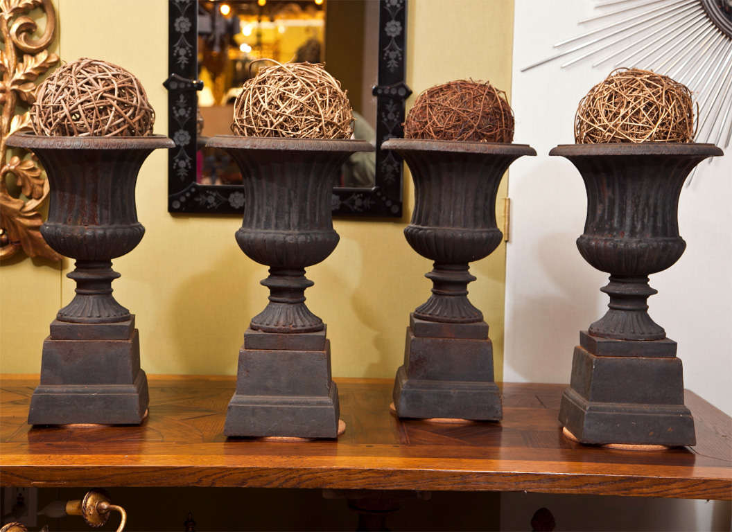 Set of four cast iron Campagna style urns on pedestals.