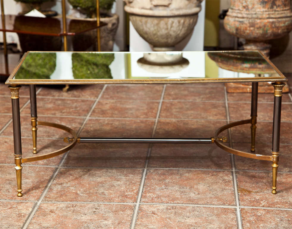 Maison Jansen neoclassical gilt bronze coffee table trimmed in brass, inset with mirrored top and raised on round legs, joined by bowed stretcher.