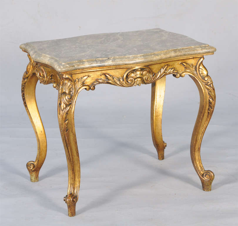 Table, having a marbelized rectangular molded top with bowed sides, on conforming base of giltwood, its foliate carved apron centered by cartouche, raised on acanthine cabriole legs with scroll toes.