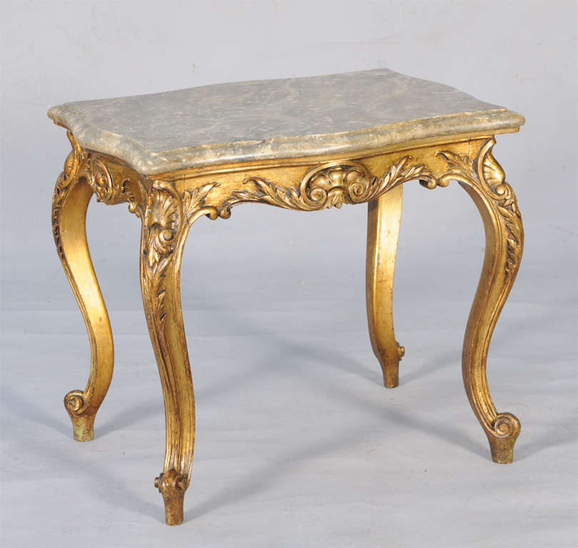 Table, ayant un plateau rectangulaire mouluré marbré avec des côtés arqués, sur une base conforme de bois doré, son tablier sculpté de feuillage centré par un cartouche, élevé sur des jambes cabriole acantines avec des pieds de rouleau.