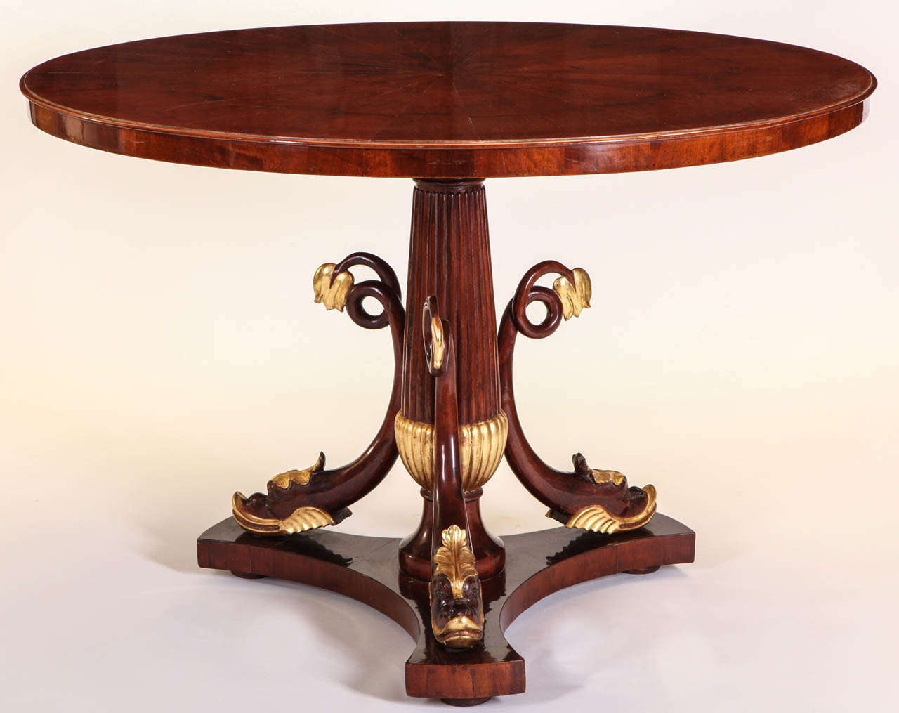 An Italian mahogany and parcel-gilt centre table with a circular top above triple addorsed dolphins on a triform base,

Tuscany, 1830.