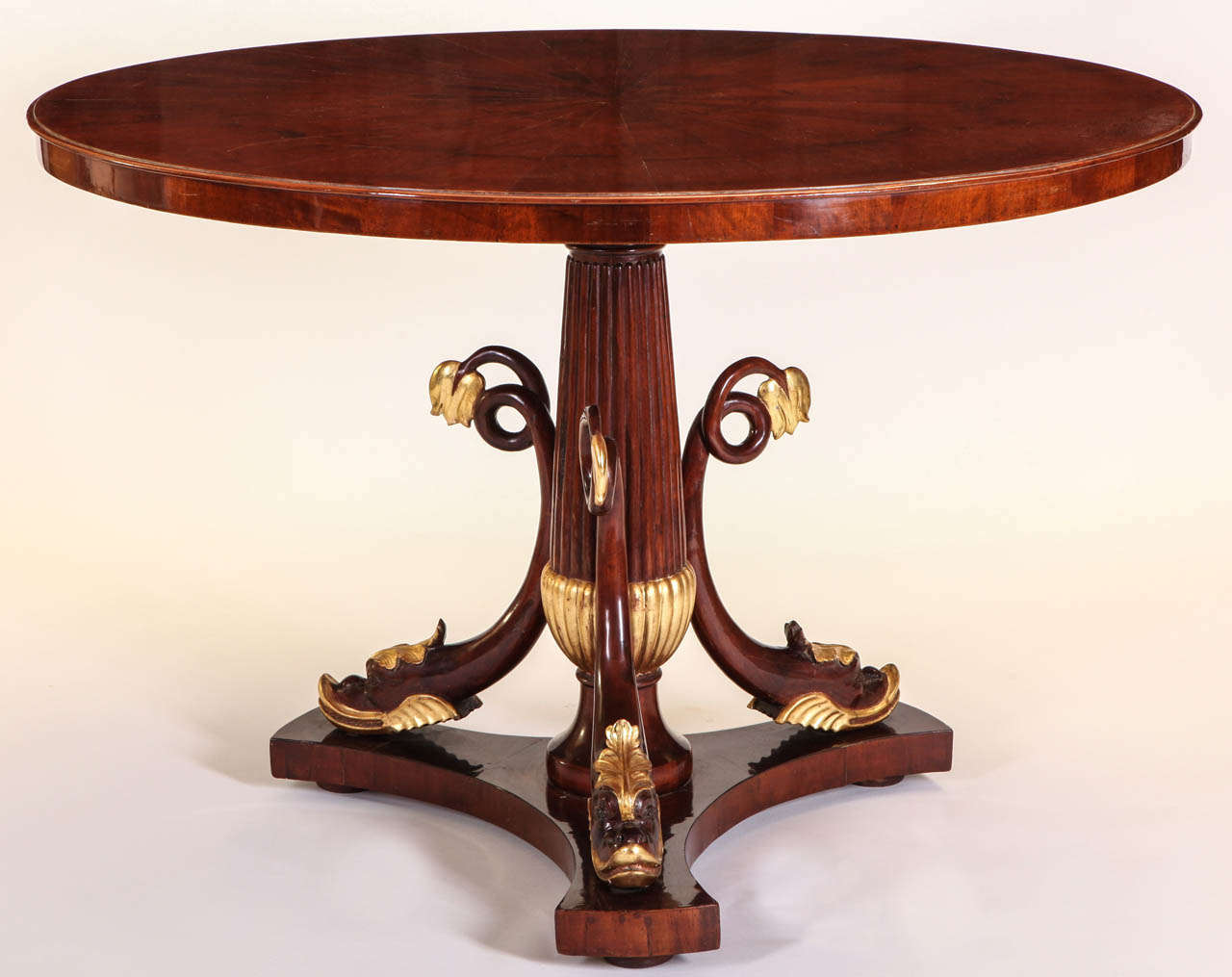 Mesa de centro italiana de caoba y paquetería dorada, con tablero circular sobre delfines de triple adorno y base triforme,

Toscana, 1830.