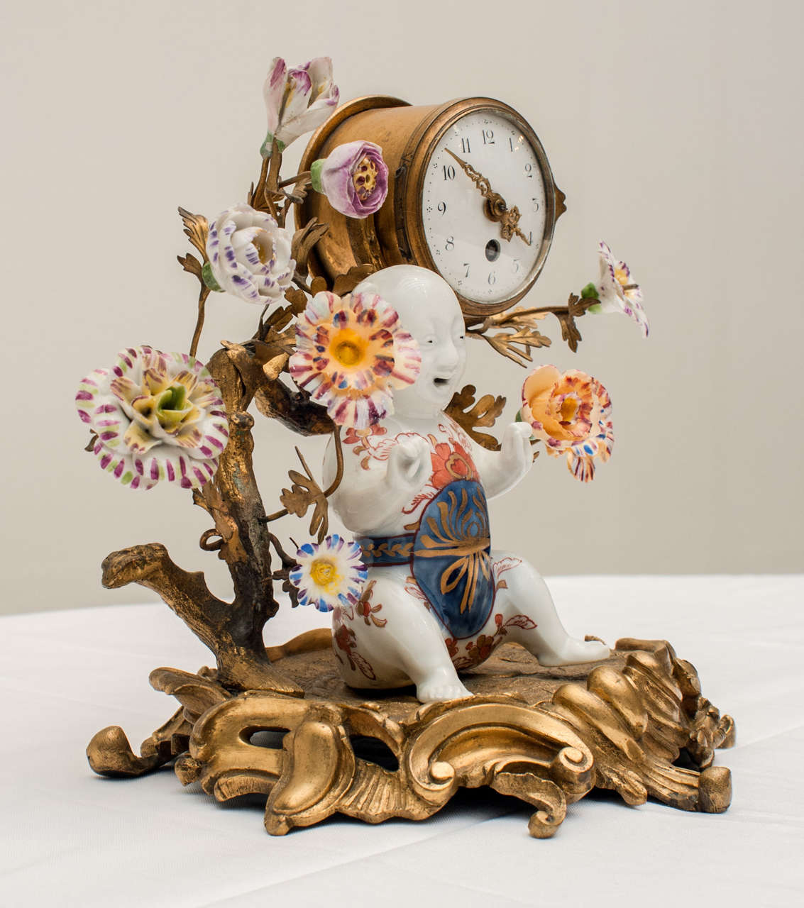 A small Chinese porcelain and gilt bronze clock. It features a nice decoration in the spirit of rococo with foliate scrolls. The gilded branches and sheet metal leaves are decorated with multi colored porcelain flowers surrounding a young child<br