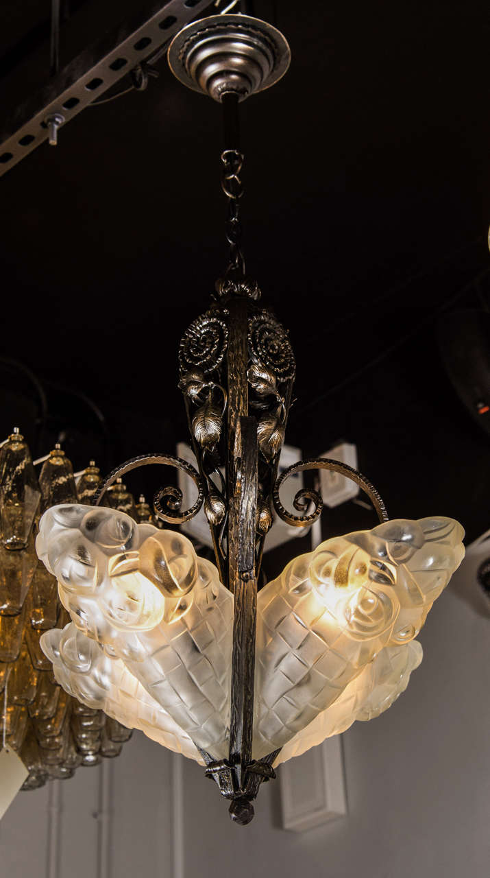 This elegant chandelier features a handmade wrought iron frame with a design of scrolling tendrils and fauna all done in the manner of Edgar Brandt. The chandelier is fitted with four relief frosted glass shades with stylized Art Deco geometric and