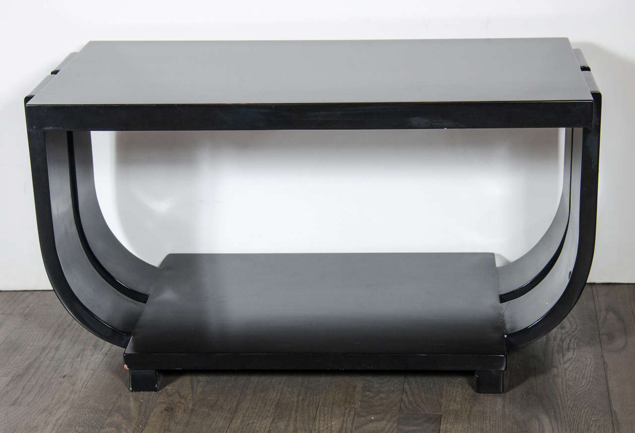 Machine Age cocktail table in a black lacquered finish, it has stylized double banded curved sides with a lower tier, and floating based legs. This piece has been mint restored.
