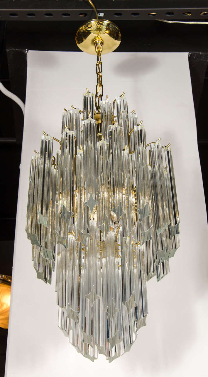 This elegant Mid-Century Modern Camer chandelier was realized in Italy, circa 1970. It features three tiers of elongated and staggered cut glass triedre rods- imbuing the piece with a unmistakable dynamism and verve- attached to a brass frame.  With