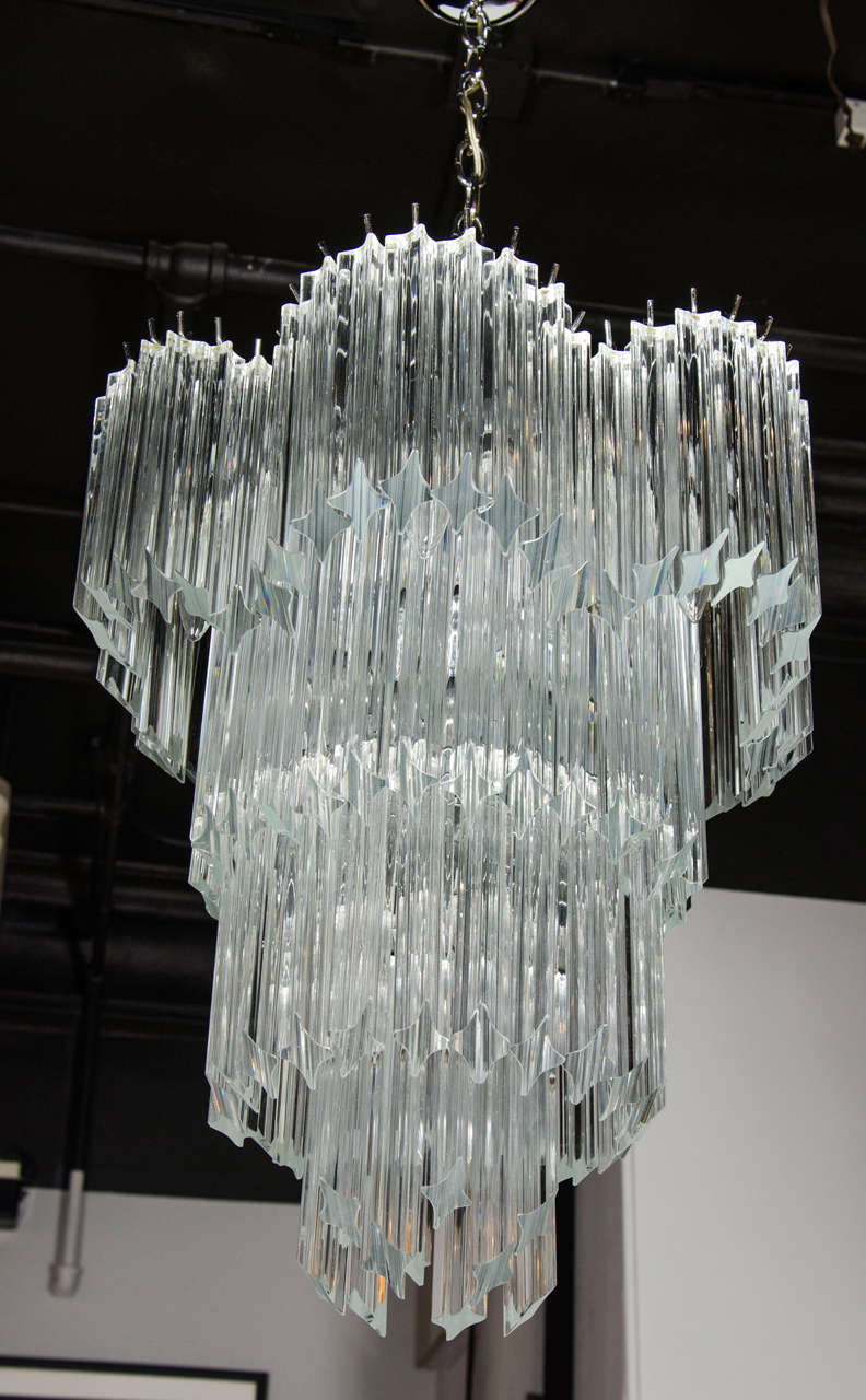 Mid-Century Modernist four-tier cut triedre crystal Camer chandelier. This chandelier features four-tiers of individually hung crystal triedre Camer rods. The top-tier features a scalloped designed border, giving the chandelier great dimension. The