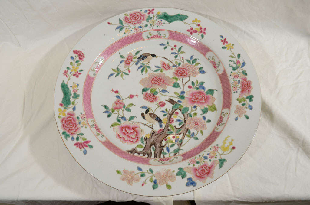 A large Famille Rose Chinese export charger with soft pastel colors, predominant pinks, with greens, yellow, and blue. The hand painted scene shows song birds in a flowering tree surrounded by peonies. These pastel colors came into use in China soon