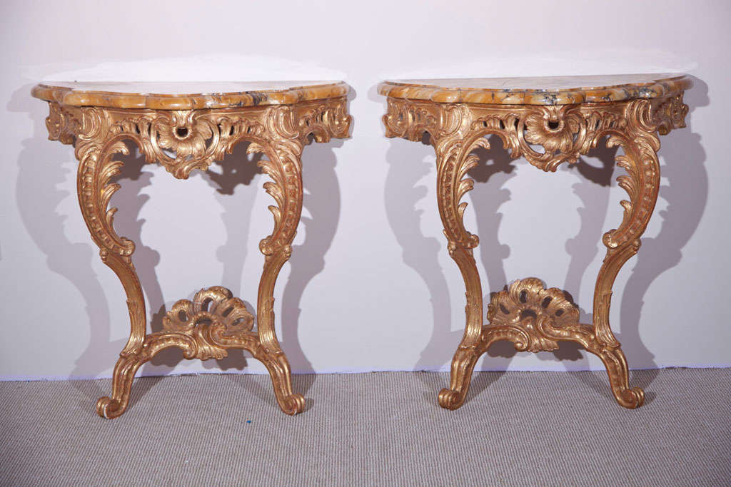 A fine pair of late 19th century Rococo marble top French gilt carved-wood consoles with leaf and shell motifs.