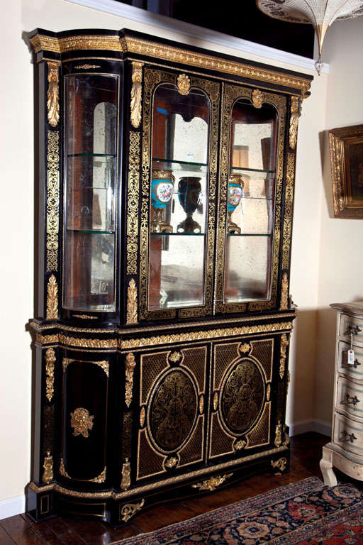 Ebonized  cabinet with overall foliate scrolled brass inlays, applied gilt acanthus leaves and masks. Double glazed doors with shaped sides and two interior glass shelves in a mirrored cabinet. The lower cabinet with velvet lining.