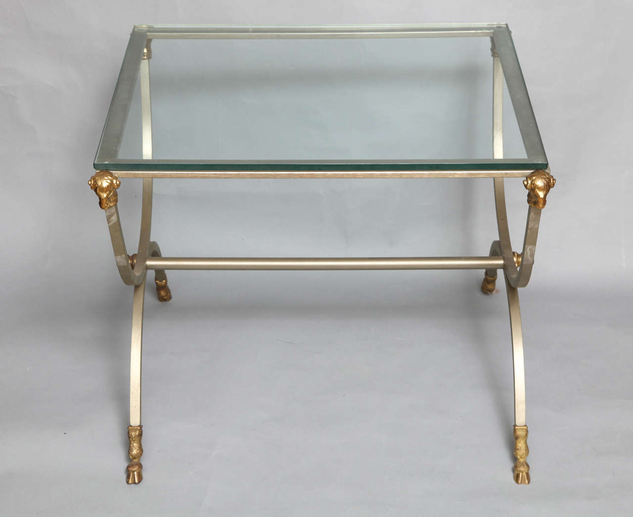 A square French steel and gilt bronze side table in the manner of Maison Jansen with X-shaped sides split hooved bronze feet and ram's heads.