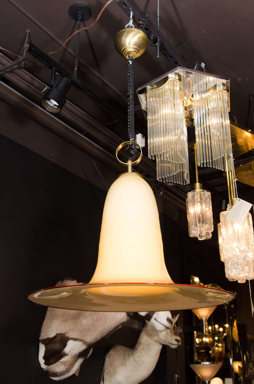 Outstanding mid-century modern large pendant light fixture with stunning elongated bell formation. Handblown Murano glass in hues of parchment with amber glass rim. Features a stylized brass ring fitting with fabric coiled cord.