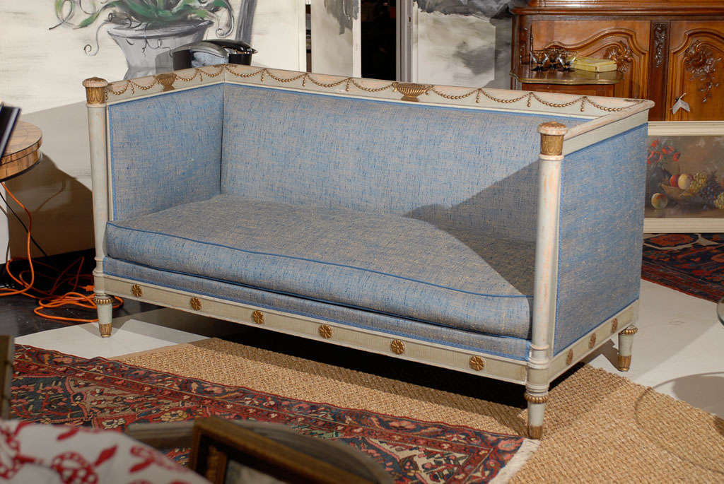 Sofa in the Swedish Neoclassical Style painted gray with gilded details and upholstered in a blue tweed fabric.  Urns and swags adorn the top rail of the sofa and rosettes adorn the seat rail.  The arm stiles are turned and have decorative gilded