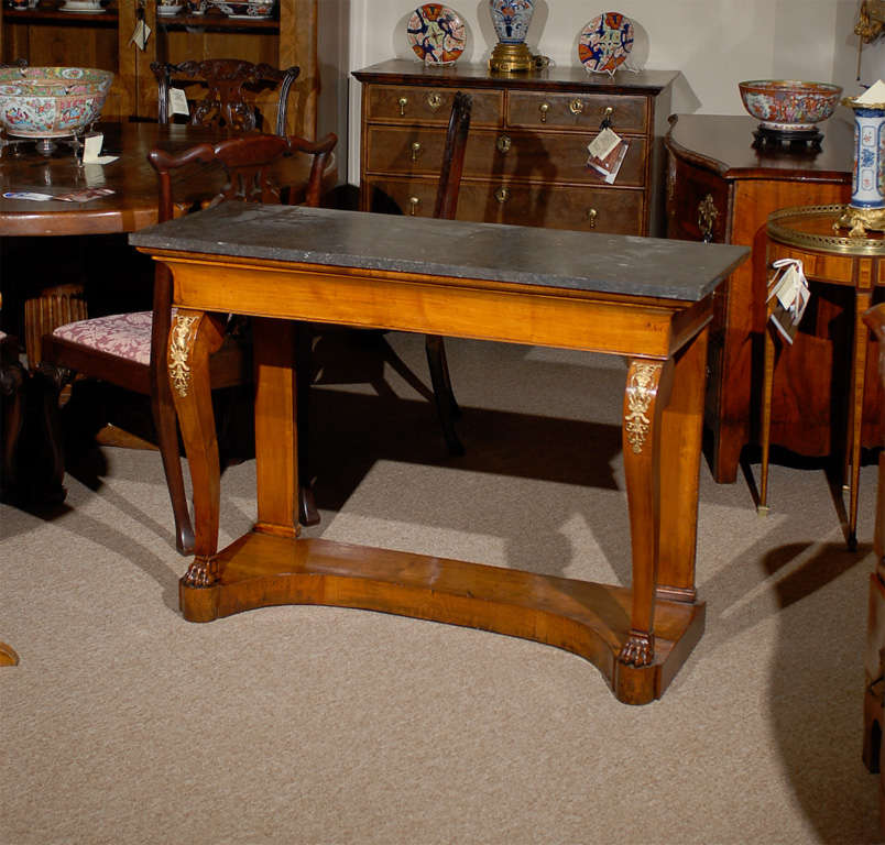 Table console Charles X en noyer avec plateau rectangulaire en marbre noir, tiroir central et quincaillerie en laiton sur des pieds courbes avec pattes. Le tout est soutenu par une base en forme de plinthe. 