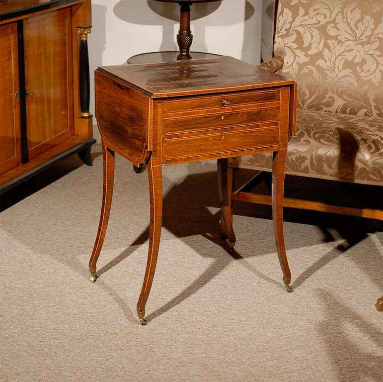 A fine Early 19th century rosewood work table with cross-banding and boxwood string inlay through out, with shaped drop leaves, 2 sliding drawers and a sewing basket below that is not shown in pictures. All resting on saber legs and castors. <br
