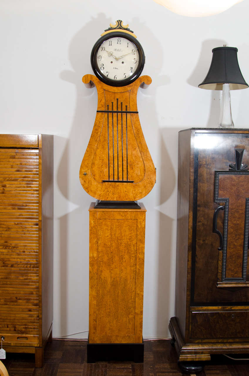 Slim and elegant, this  lyre-shaped clock case of nordic and karelian birch, is a classic example of the Biedermeier period ,from the Swedish town of Mora.  A well-preserved, hand-painted face wearing a gold and black crown, rests upon a lyre shaped