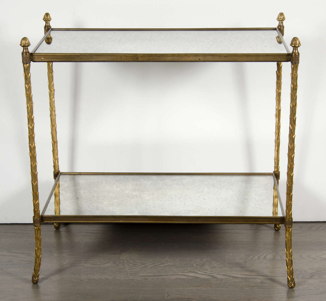 This luxurious Bagues Gilt Bronze two-tiered table features a frame in a stylized foliage design in a naturalistic form with tapered legs and antiqued mirror shelves.