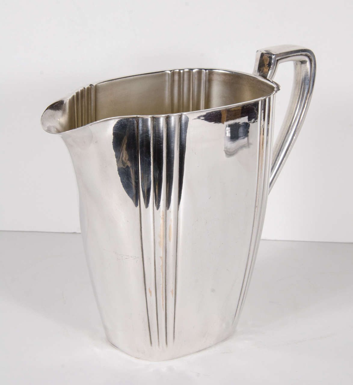 This stunning pitcher features a Art Deco style ribbed detailing with a stylized neoclassic handle.This pitcher is made of fine silver-plate and bears the name Rogers Company on the bottom.
