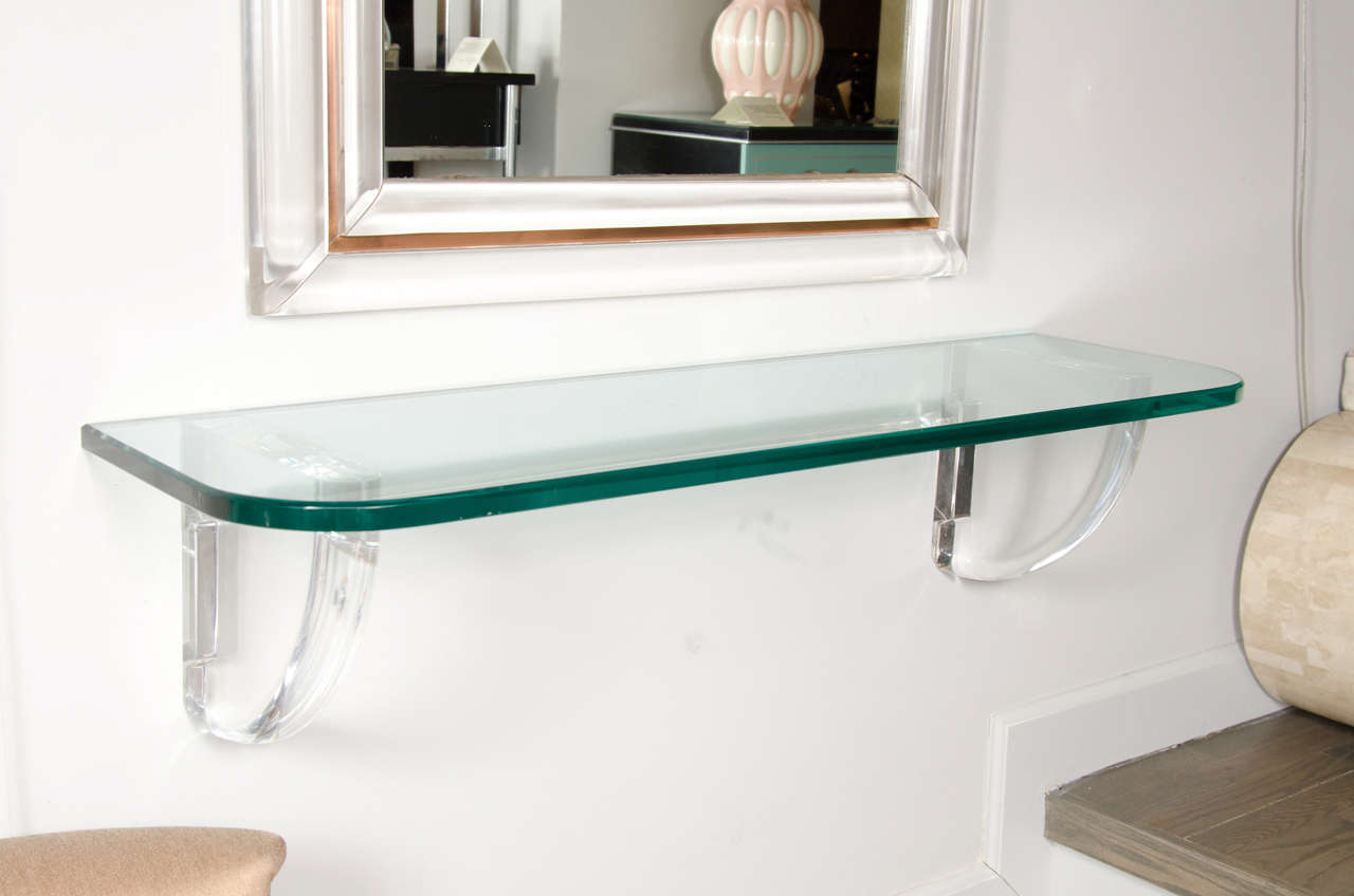 This Mid-Century modernist curved wall shelf with clear thick lucite supports and thick glass top seem to float from the wall because of its brilliant design. This piece is in mint vintage condition.