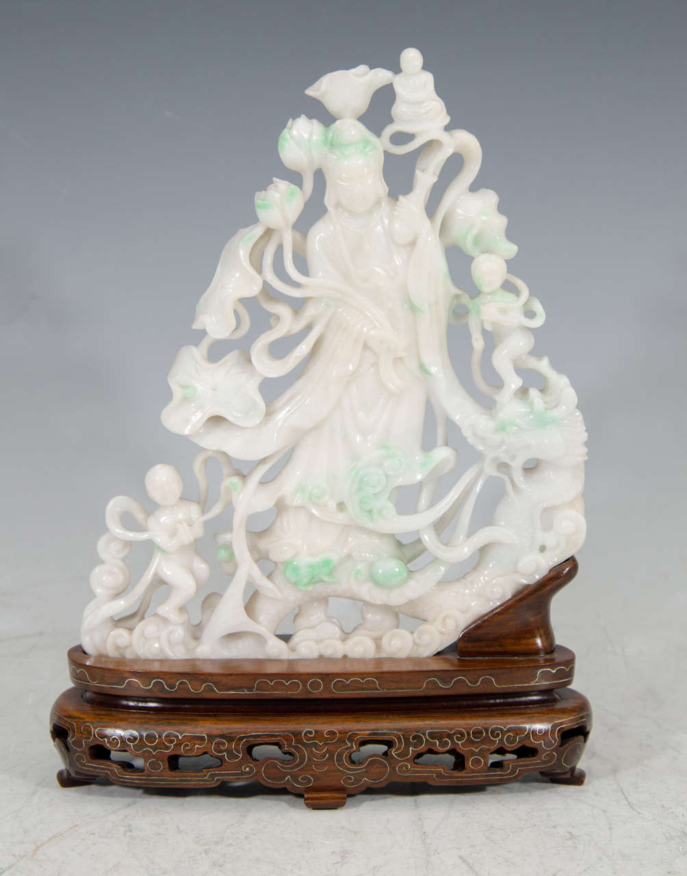 A Chinese sculpture of a Guanyin with golden boy and golden girl (Chinese Buddhist History) in green and white jadeite. This piece sits on a carved wood base with inlaid silver.

Measurements: 10 3/4