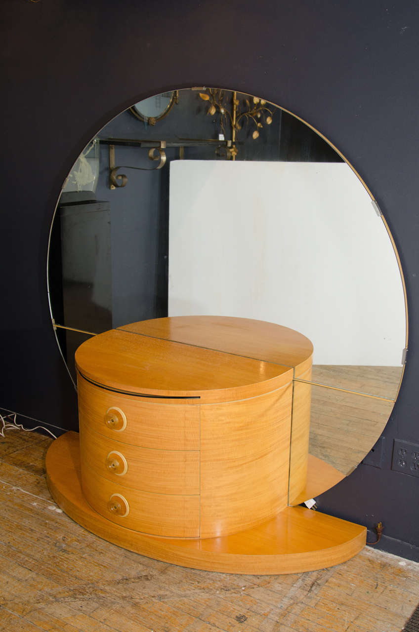 An Art Deco vanity or dressing table, circa 1930s in beechwood with large round mirror, curved drawers, apple juice bakelite hardware and single glass insert that pulls out for cosmetic items if desired.

Good vintage condition with age