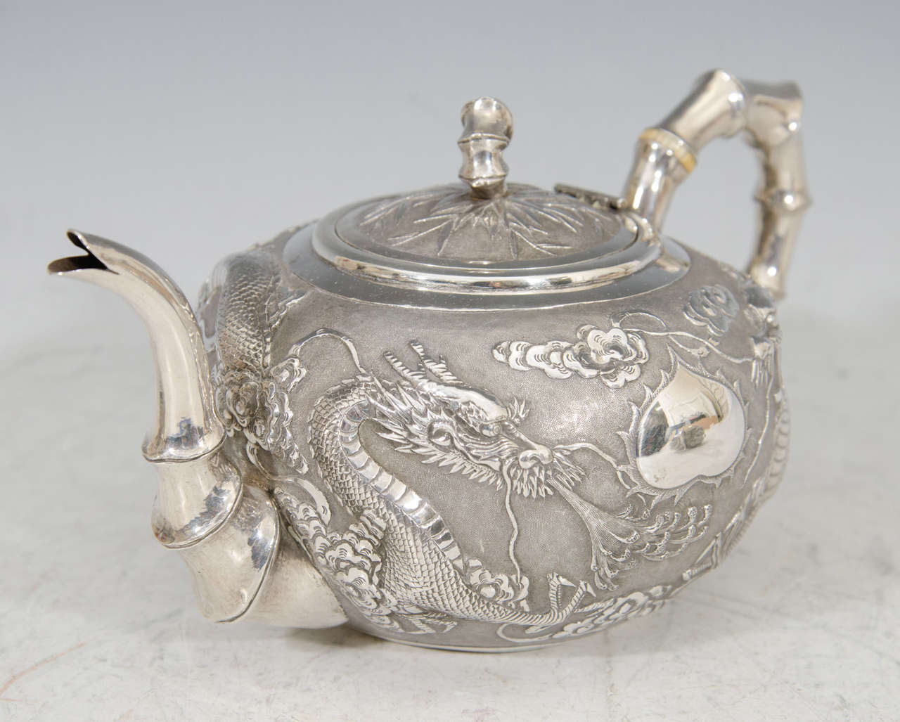 A finely worked Chinese export tea set in silver decorated with two dragons chasing a ball. Each piece has a faux bamboo handle and spout. Clearly marked Wang Hing.

Good condition with age appropriate patina.

Measures: Creamer 5.5