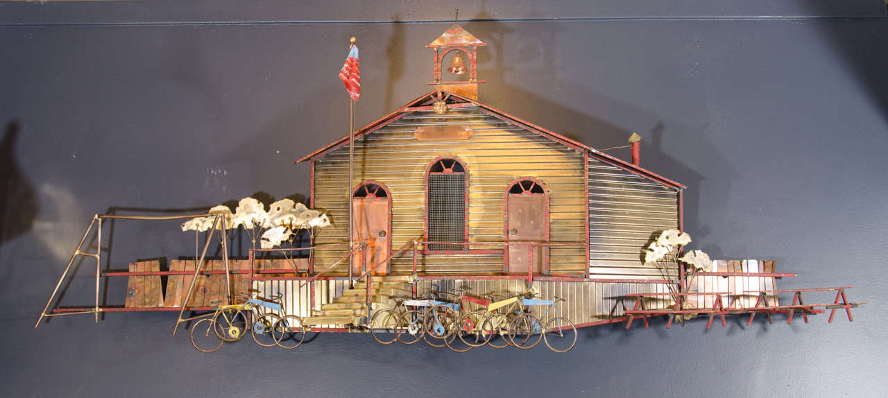 A terrific vintage mixed metal hand-painted wall-mounted sculpture of a schoolhouse with ringing bell, flags, bicycles and picnic tables.