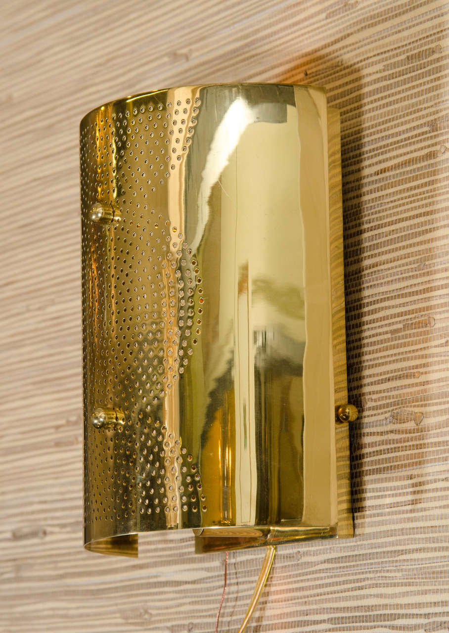 A contemporary wall sconce in brass with perforated circle design.