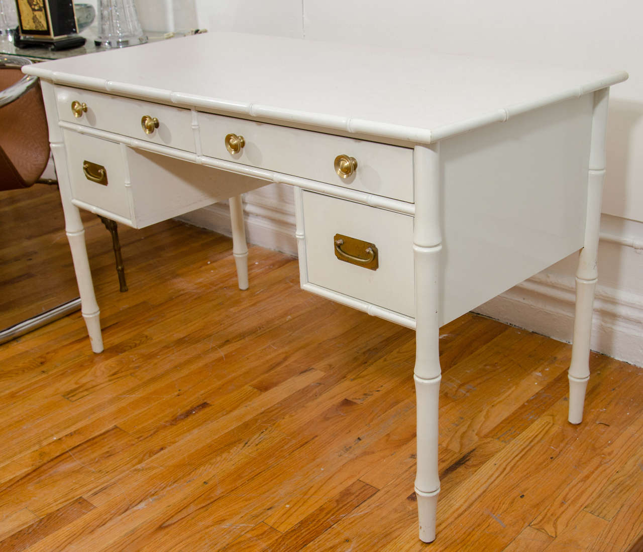 A Hollywood Regency style desk with white paint over wood, faux bamboo motif and brass hardware. Good vintage condition with age appropriate wear and patina. Some scuff marks.