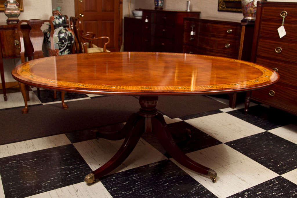 This oval table, though described as a breakfast table, is also a suitable dining table for a small apartment. It is a pale, honey toned mahogany with multiple exotic wood bandings, the largest of which is a satinwood band having a hand-painted