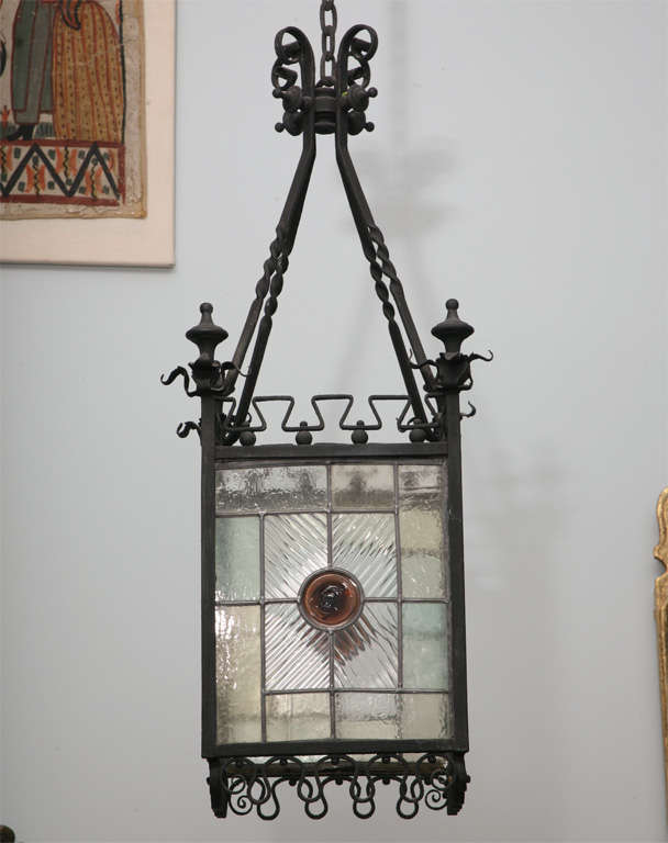 Fine English Arts and Crafts wrought iron and leaded stained glass hanging hall lantern, the frame finely wrought of heavy gauge iron, with turned finials over four geometric sides with amber center bosses and having filigree wrought iron borders on