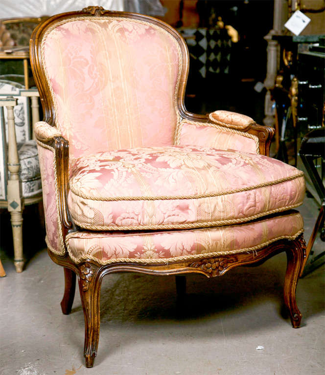 Pair of French Louis XIV style walnut bergere chairs, circa 1940s, the round back with rosette-carved crest to down-swept, padded arms, upholstered in silk fabric, cushioned seat, raised on cabriole legs.