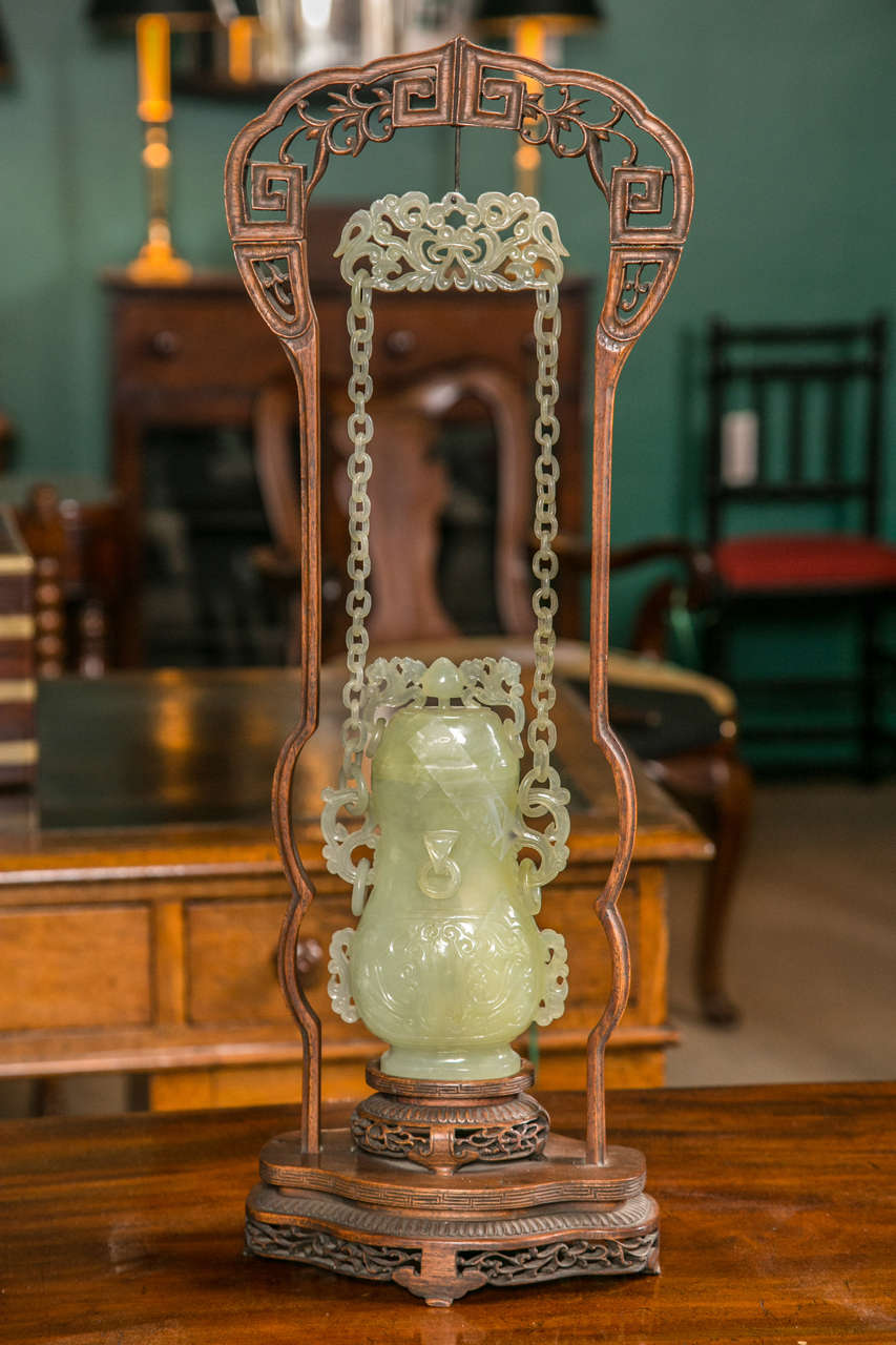 A Chinese carved Bowenite jade chain vase. The chain, vase and cover all carved from one piece. Four loose rings on vase, two on cover, custom-made carved wood display stand.
Dimensions of jade piece : 15.5