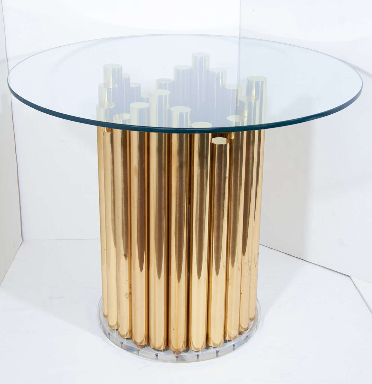 Modernist table with sculptural form comprised of a tubular brass pedestal base with thick circular lucite support and glass top. The table base has a skyscraper design with brass cylinders at alternating heights.  It can be used as either a center