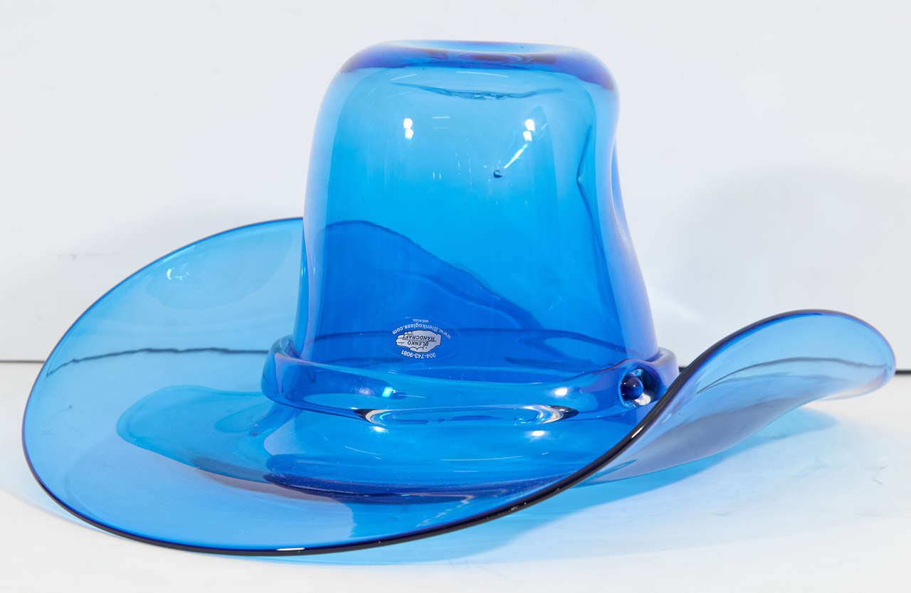 A western style broad brimmed hat in blue glass by Blenko. The piece may function decoratively or be used as an ice bucket. Markings include signature and date [Richard Blenko, 2000], etched to the top of the hat, as well as the original sticker