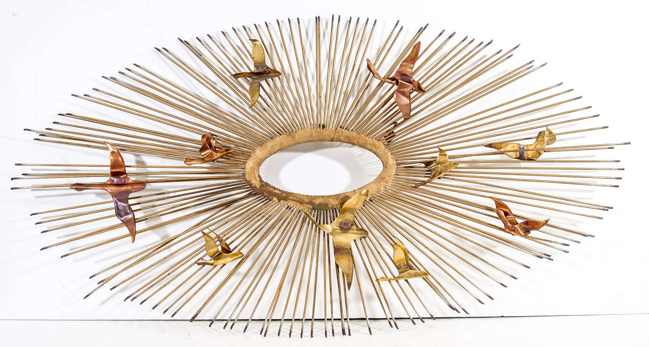 A vintage brass and copper wall sculpture of a sunburst with birds in flight. The piece is unsigned but attributed to Curtis Jere.