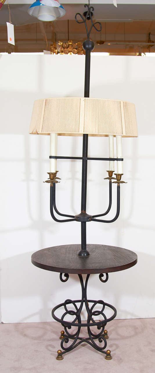 A pair of tall lamps in iron with brass detail and a circular wood table surface. They are in the attributed to Tommi Parzinger. They are in vintage condition with age appropriate wear; some scratches to wood and metal; burns on the interior of