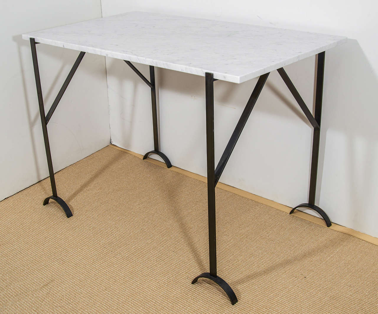 A vintage marble top table with black steel trestle legs and crescent feet