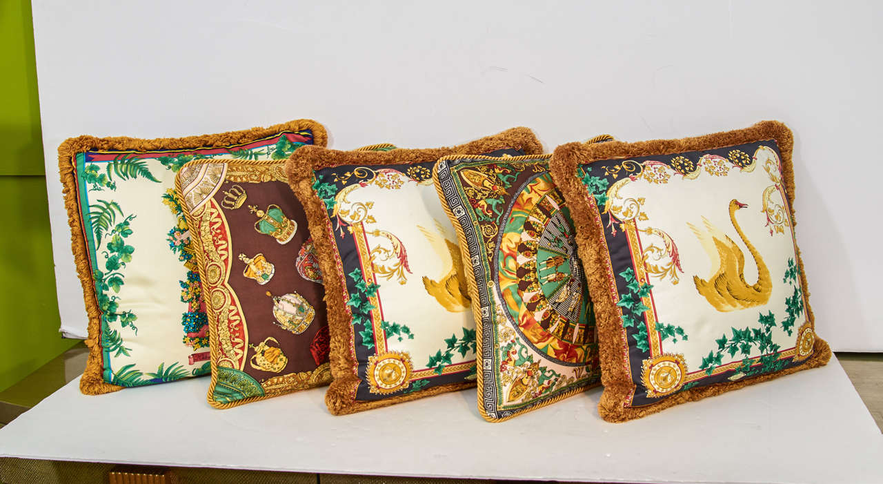 A set of five Versace double sided Baroque style silk pillows with copper brown fringe. Two matching pillows depict golden swans surrounded by an ivory motif and say, 