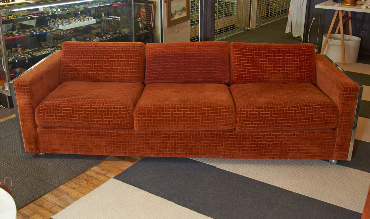 A vintage burnt orange velvet sofa with a chrome Greek key design at each end. The piece is in the style of Milo Baughman. It is in good vintage condition with age appropriate wear to upholstery (likely original)