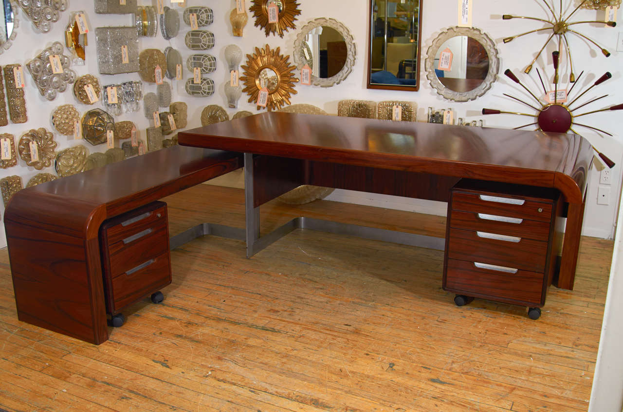 An Incredibly Designed Striated Danish Rosewood and Brushed Steel large streamlined desk with a long side table that nests beneath one end and two file cabinets on casters that nest beneath the desk and side table. Configuration of pieces can be