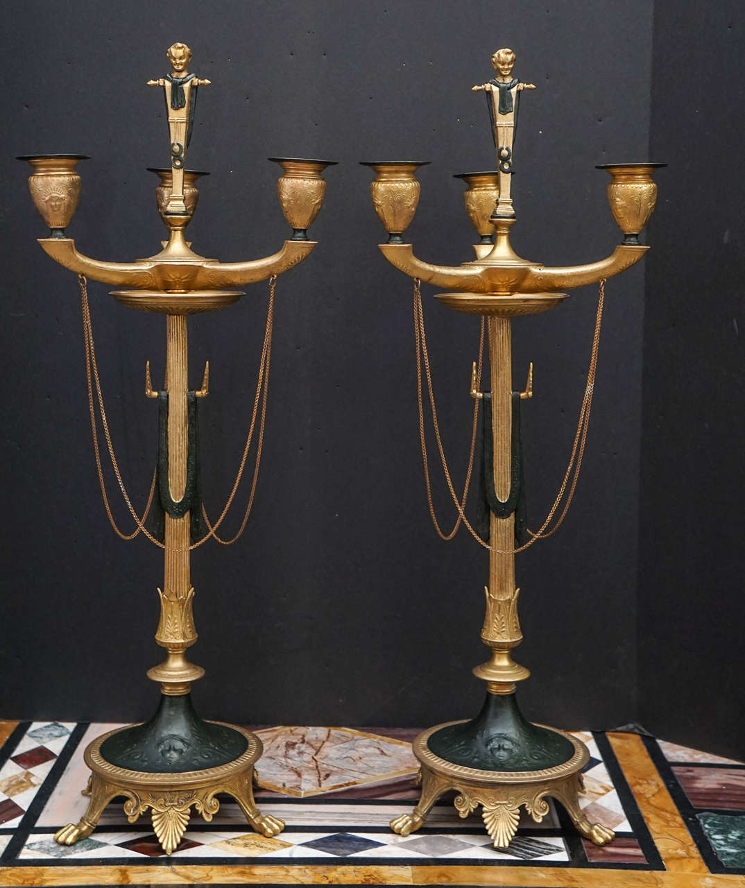 This fine and interesting pair of candelabra are from the late 19th century and are most likely French made from iron, the three light pair show both classical Greek design as well as Assyrian and Roman elements. Unusual styles were considered all