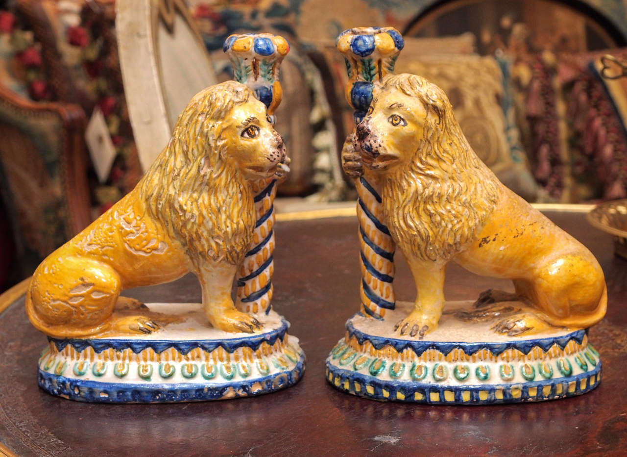 Pair of 19th century Italian faience candlesticks with lions seated holding torch form repository for candles. All on a decorated oval base.