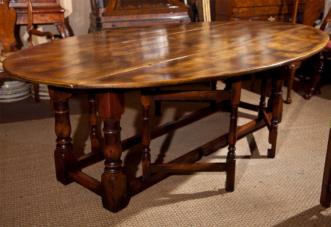 DISTRESSED FINISH OAK OVAL DROP LEAF DINING TABLE WITH 2  GATE LEGS ON EITHER  SIDE. CROSS STRETCHERS, BLOCK AND TURNED LEGS