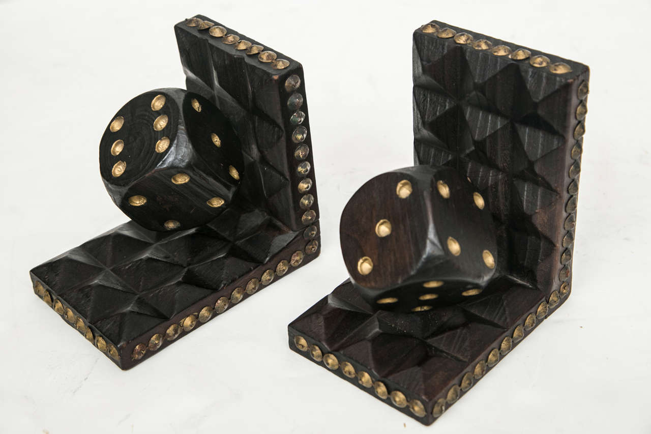 A set of hand carved wood bookends featuring dice. Brass tacks adoen the outer edges.