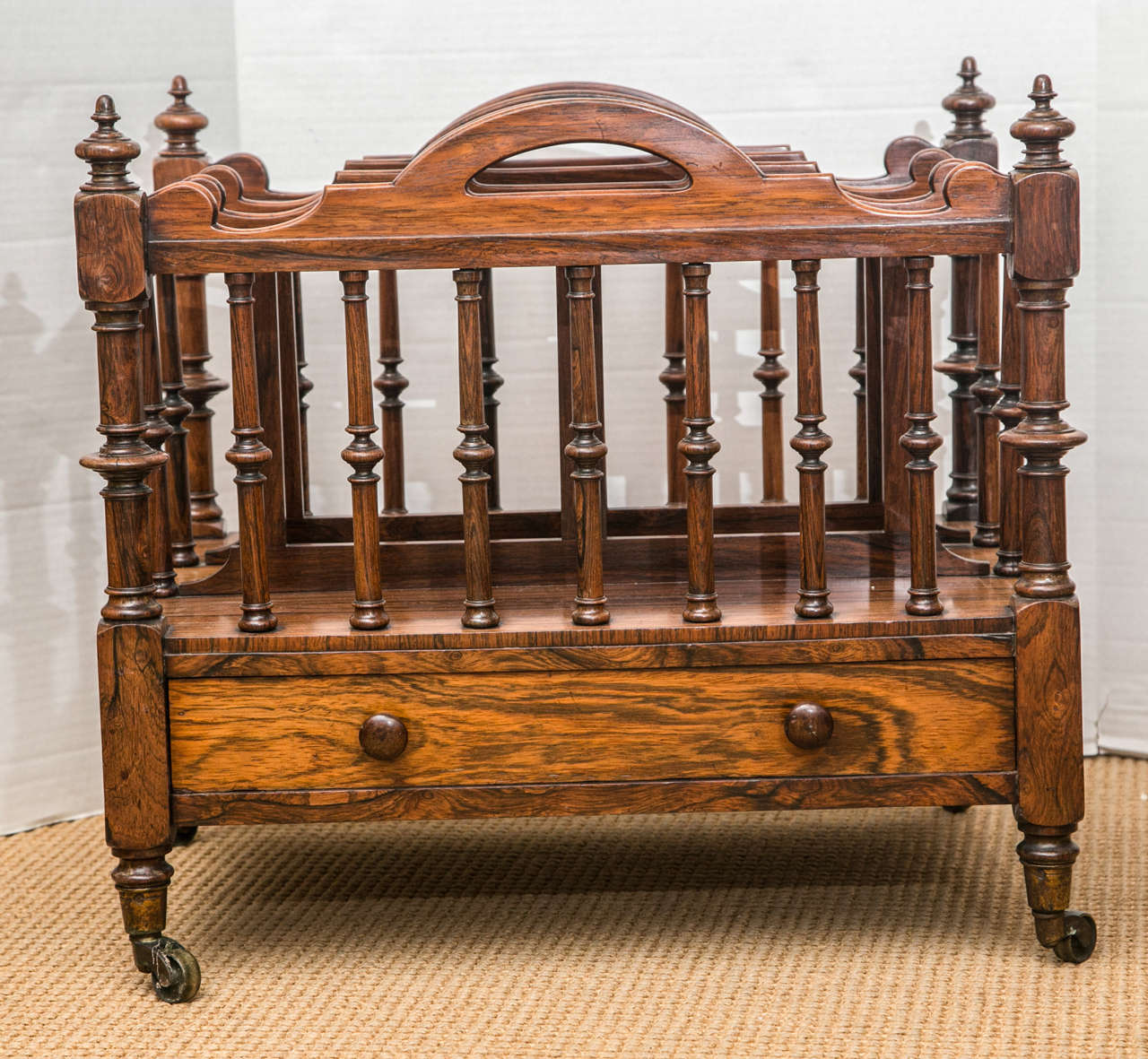 A handsome three-section Canterbury with four pierced handles, turned columns, a lower drawer, and original casters.