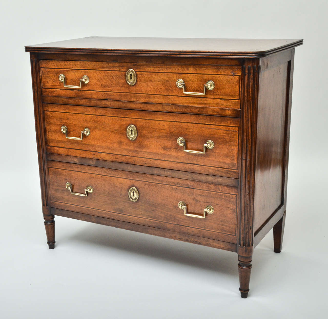 An early 19th century Italian walnut Chest of Drawers with three drawers, boxwood and ebony inlaid, reeded-molded top and brass pulls.