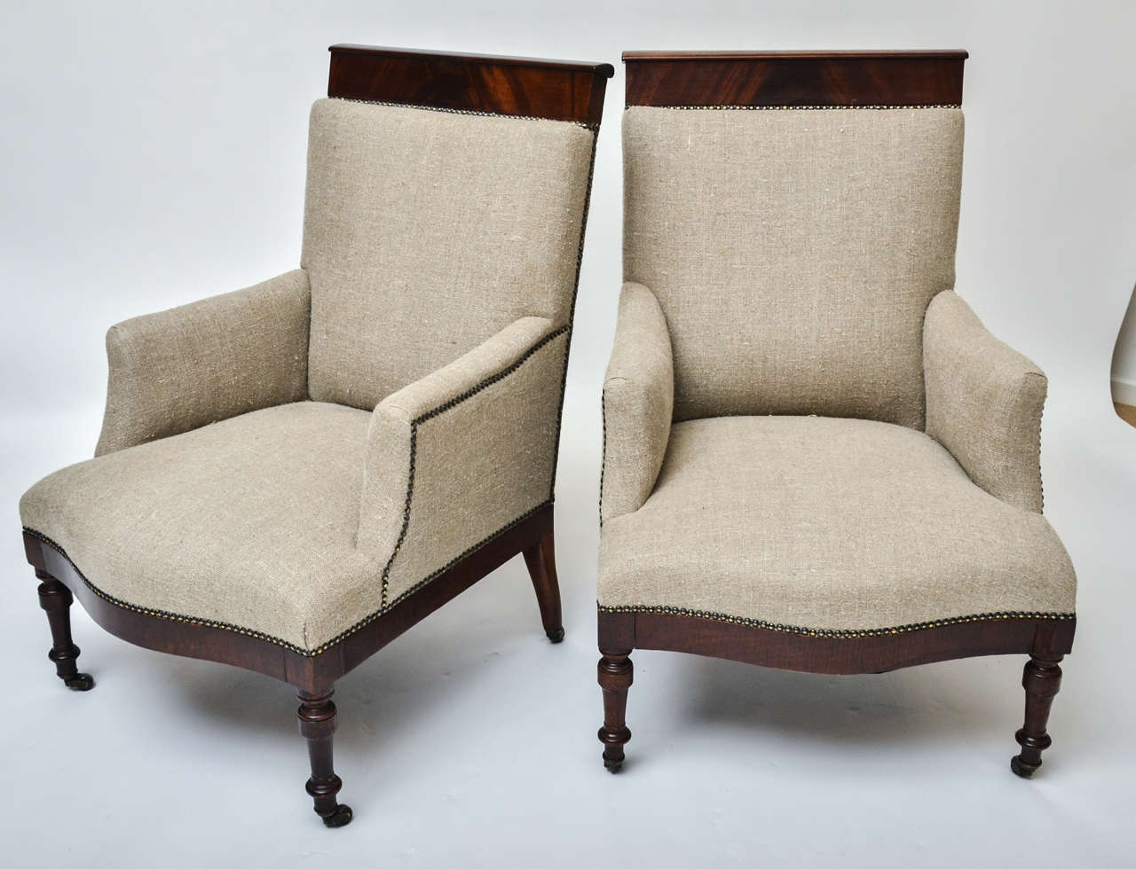 A pair of 19th century English upholstered armchairs with mahogany back rail, upholstered in beige linen, brass studs.